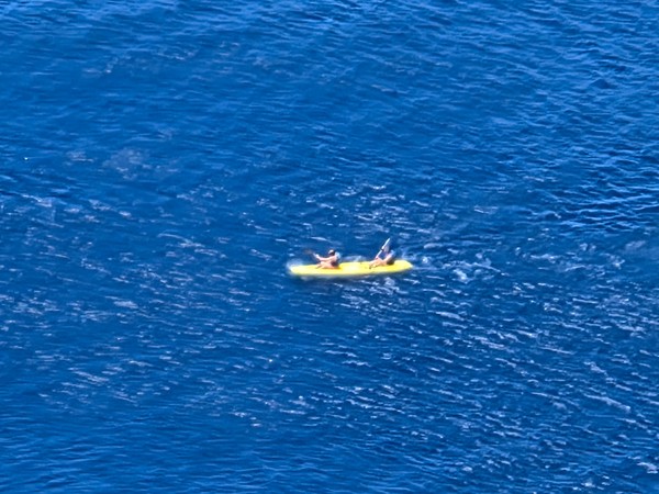 Dos personas reman en un kayak amarillo sobre el mar azul, dejando un pequeño rastro de espuma.