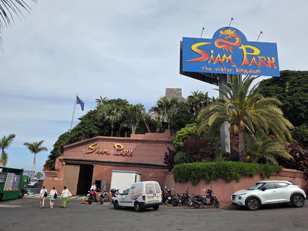 Acceso principal de Siam Park con palmeras, cartel azul y visitantes entrando al famoso parque acuático de Costa Adeje.